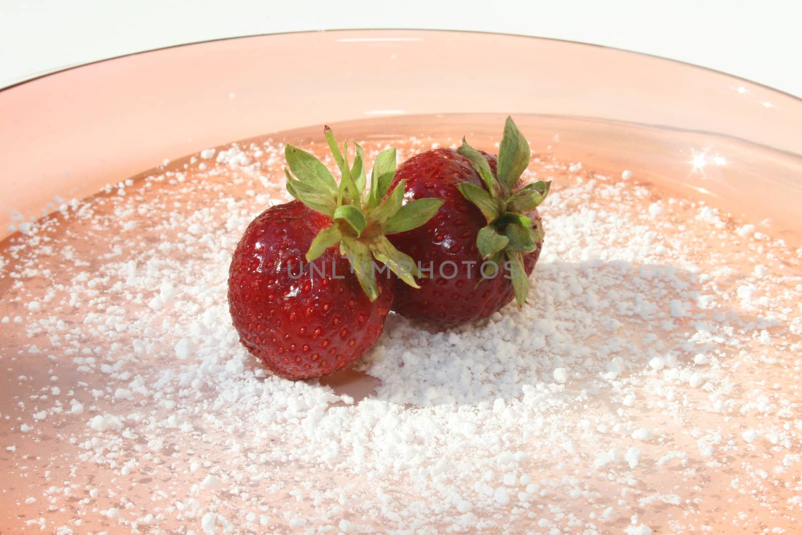 Two strawberries on powdered sugar on pink glass plate