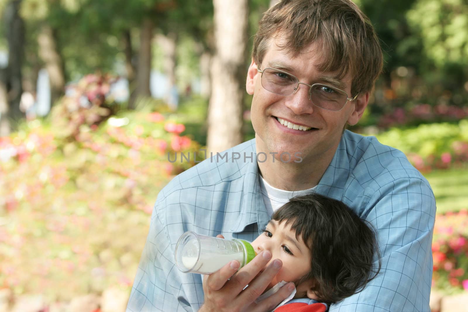 Father feeding baby a bottle in the park by jarenwicklund