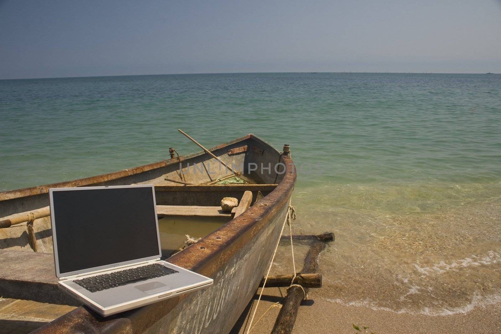 Laptop sitting on side of small fishing boat that is docked on beach