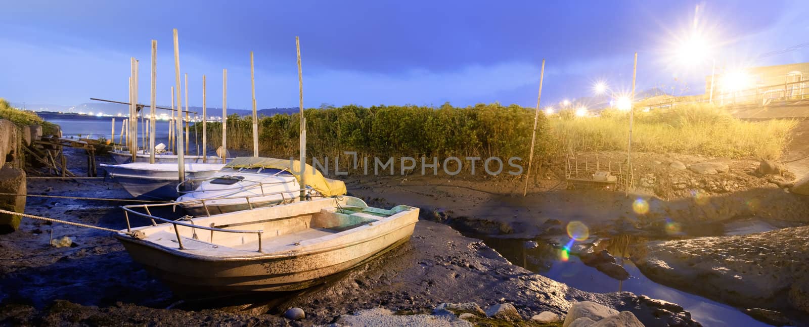 Discard boats on silt of river with city light flare in night.