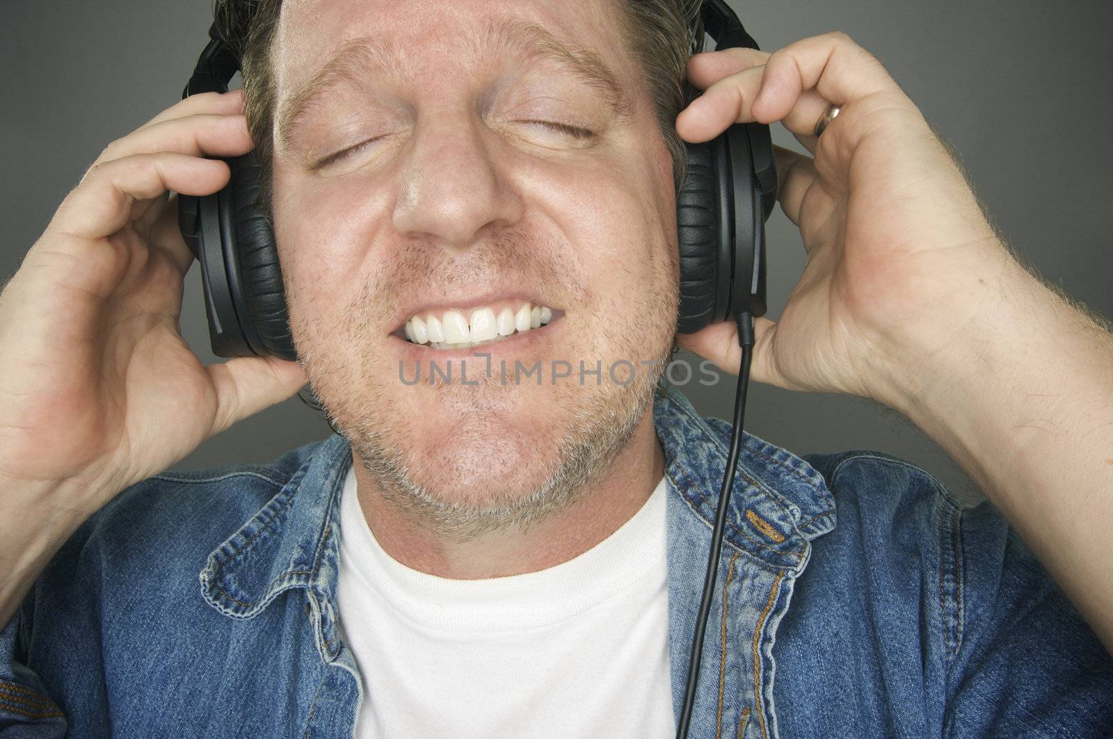 Man with Eyes Shut Wearing Headphones Enjoying His Music on a Grey Background.