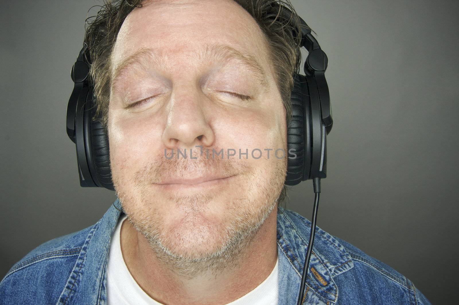 Man with Eyes Shut Wearing Headphones Enjoying His Music on a Grey Background.