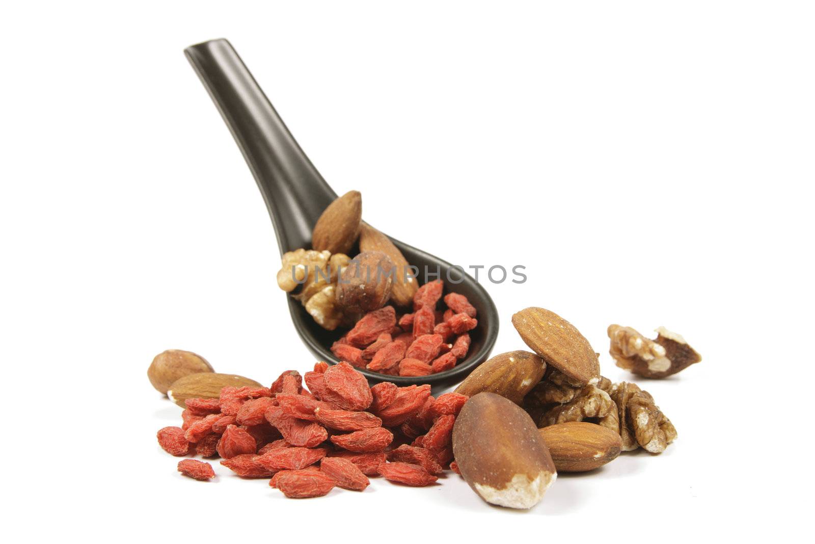 Red dry goji berries with mixed nuts on a small black spoon with a reflective white background