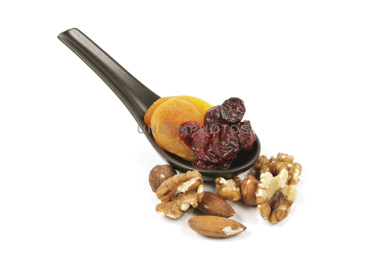 Red ripe dried cranberries and dried orange apricots on a small black spoon with mixed nuts on a reflective white background