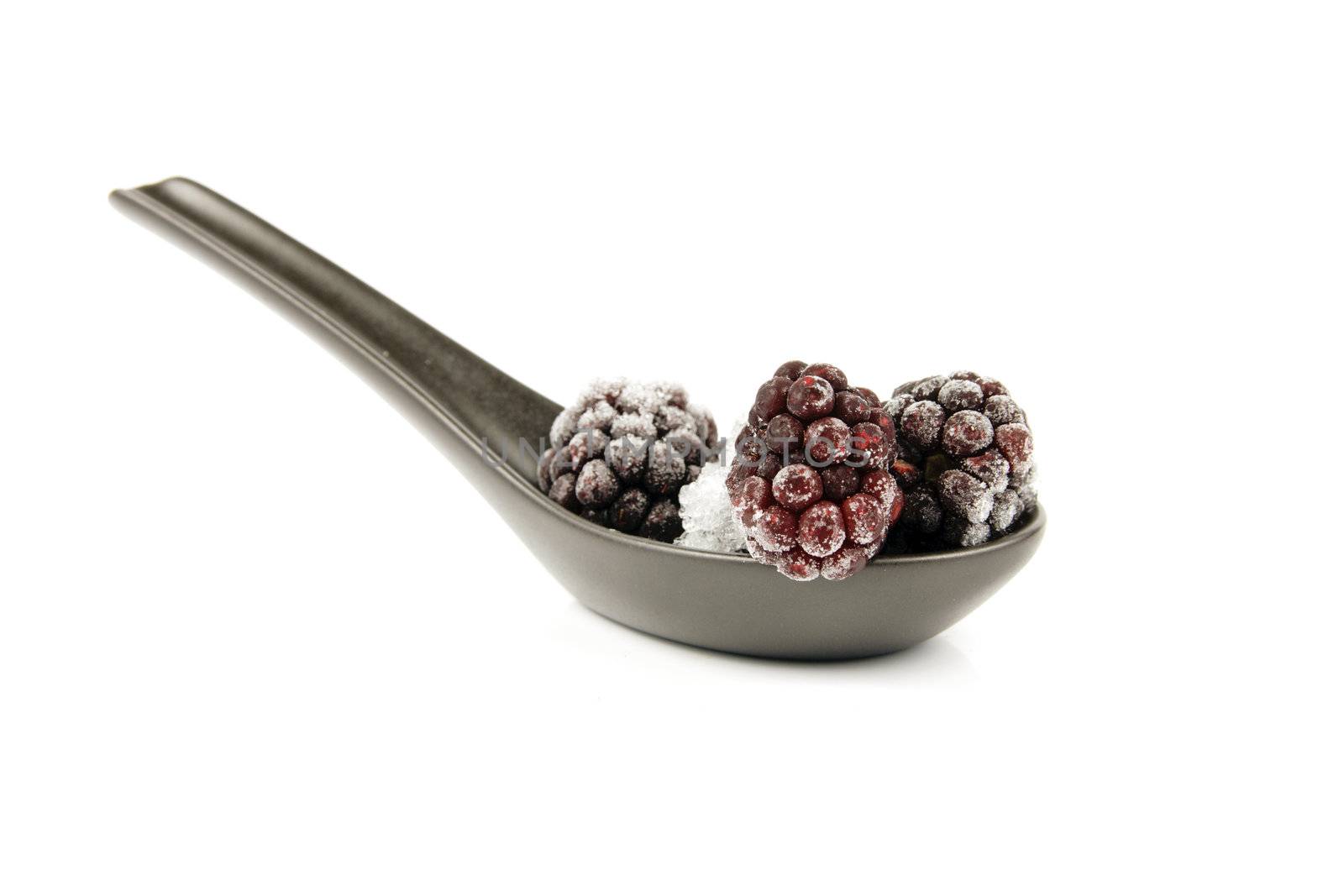 Ripe frozen blackberries on a small black spoon with a reflective white background