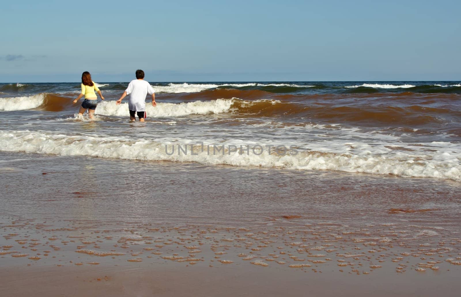 teen girl and boy walking on ocean wave at the beach