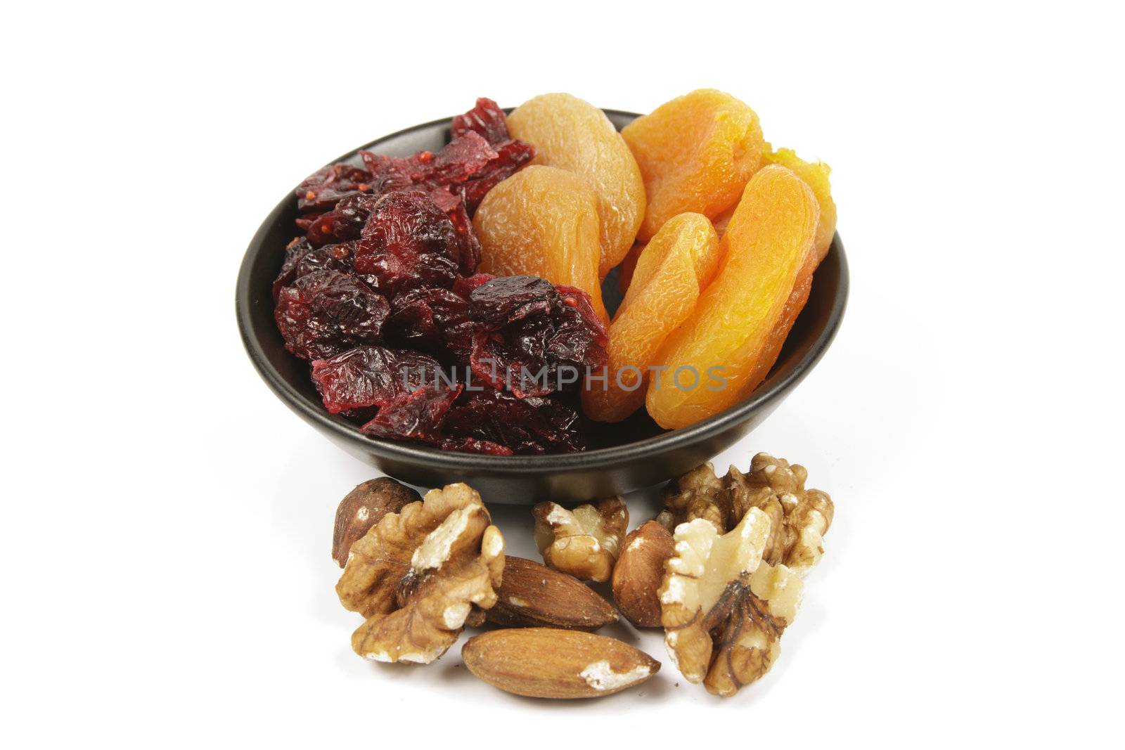 Red ripe dried cranberries and dried orange apricots with mixed nuts on a reflective white background