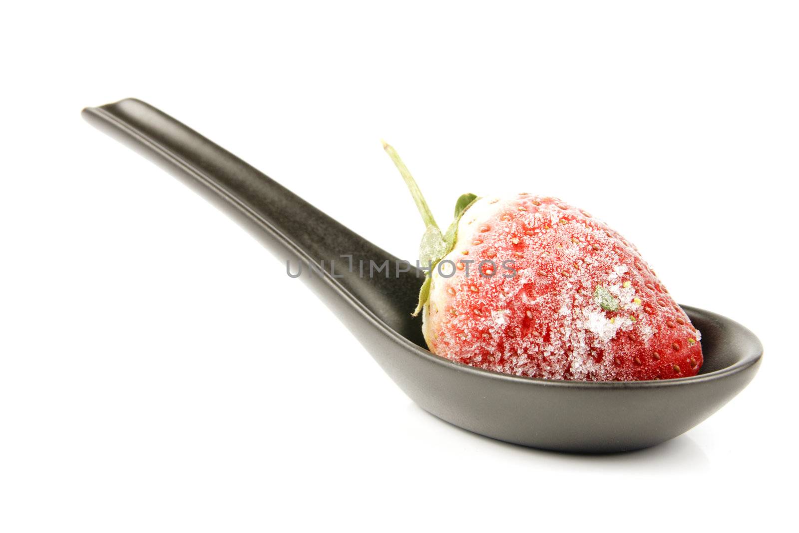 Red ripe frozen strawberry on a small black spoon with a reflective white background