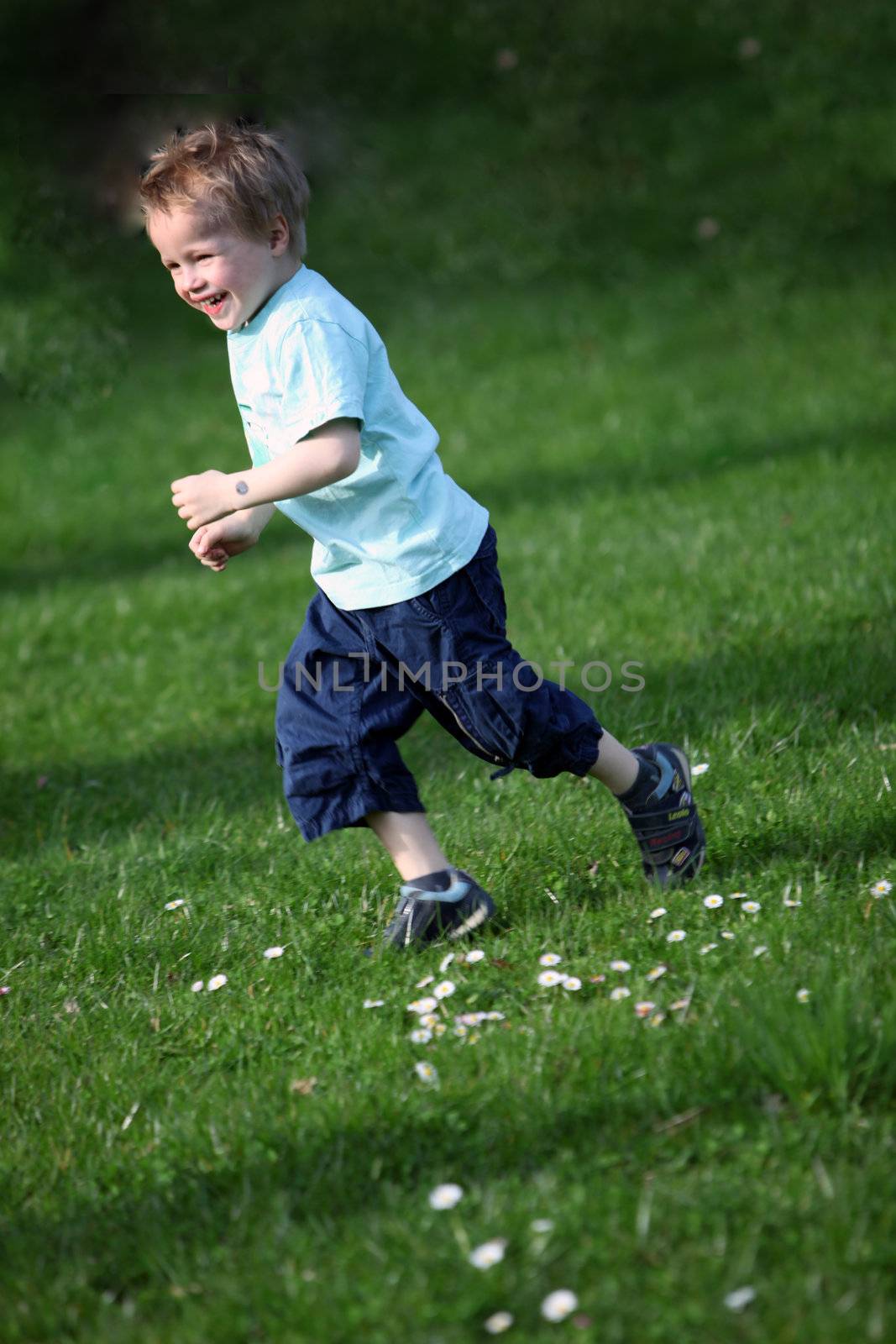 Small, blond boy running across a green meadow