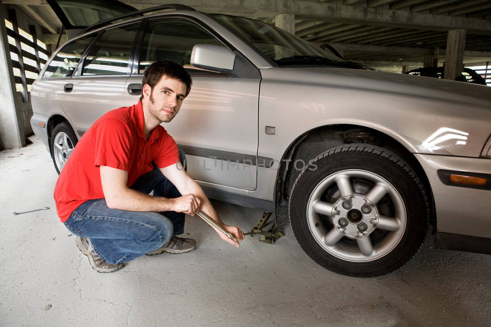 A male in a red shirt changing the front tire on a car