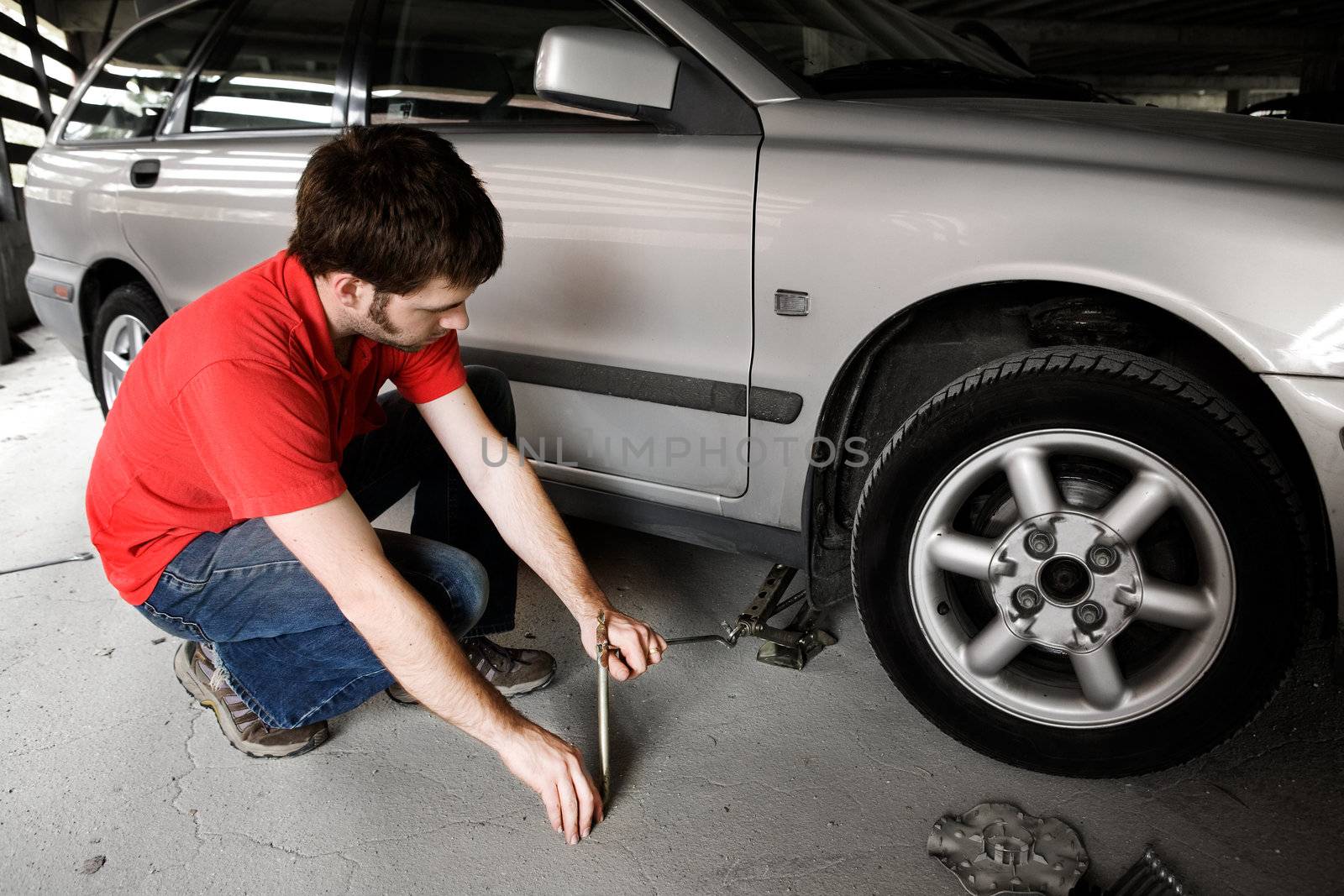 A male jacks up a car in a garage - fixing the wheel