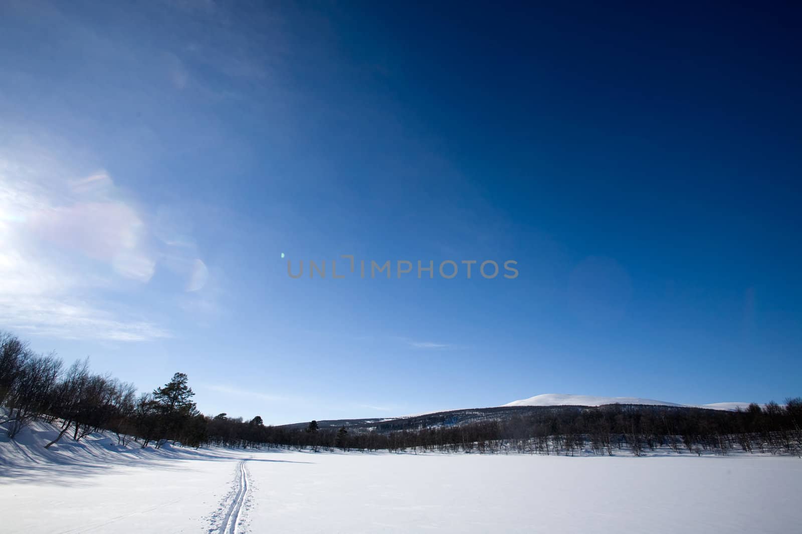 A ski trail going accross a frozen lake infront of a mountain landscape