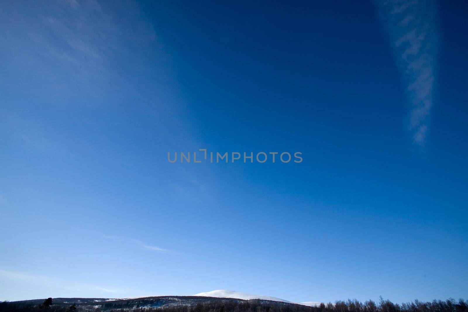 A deep blue sky background with faint clouds and a sliver of mountains