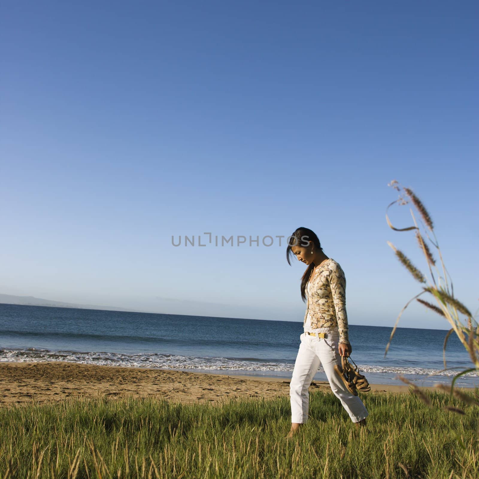 Young Asian female walking on beach and carrying her sandals.