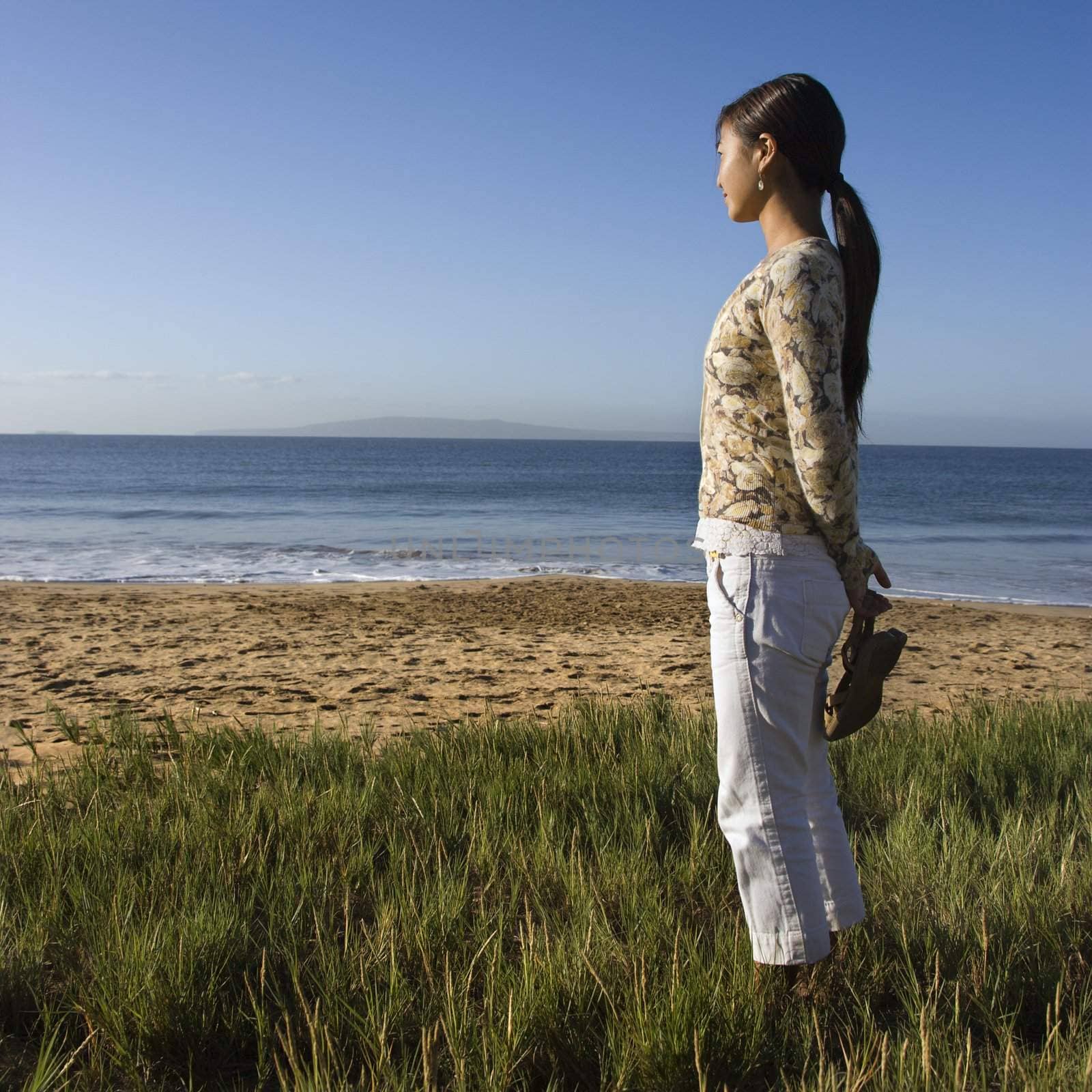 Young Asian female walking on beach and carrying her sandals.