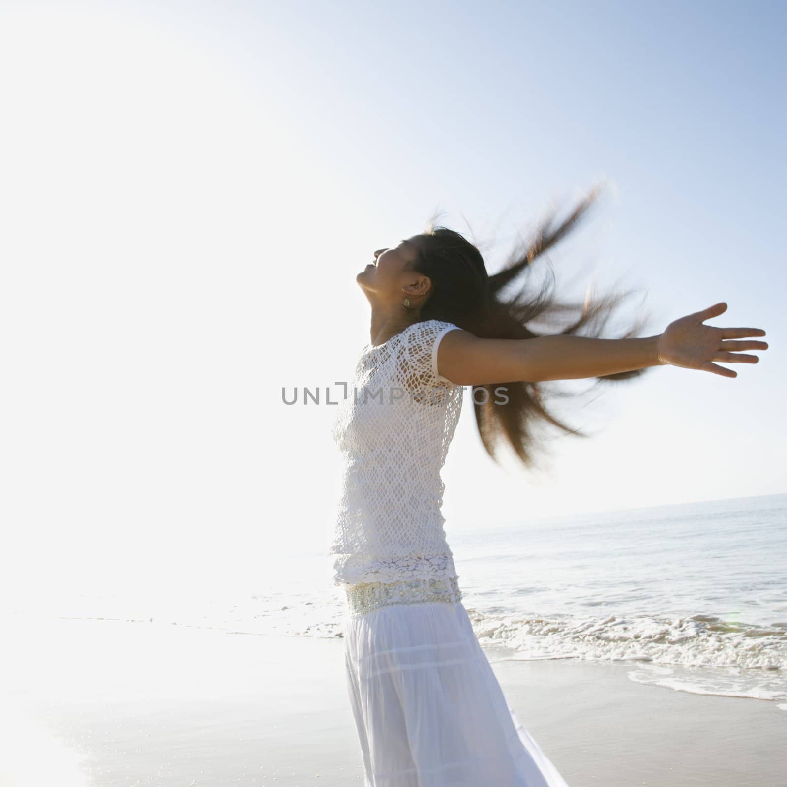 Young Asian female at beach throwing her arms back behind her.