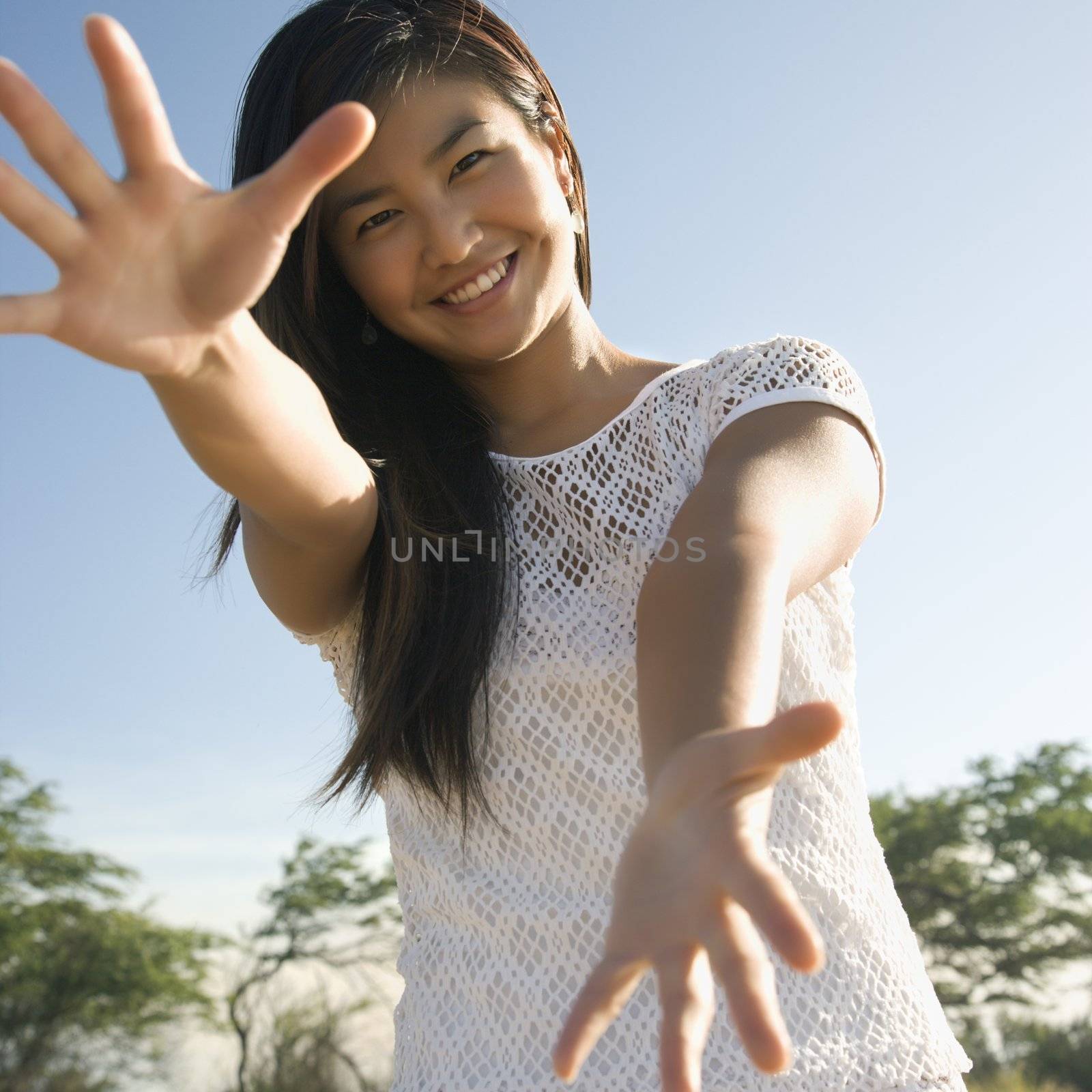 Young adult Asian female with arms and hands stretched out toward viewer.