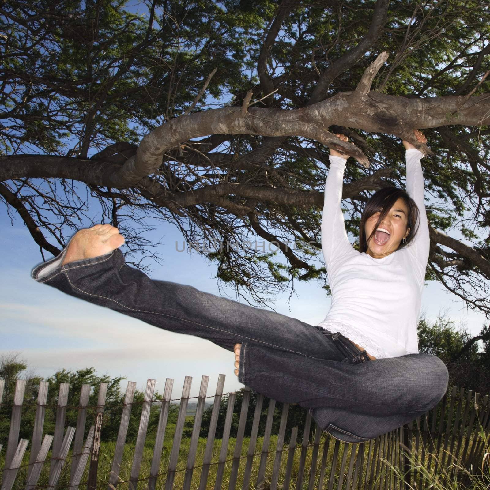 Young adult Asian female holding on to tree and kicking air and screaming.