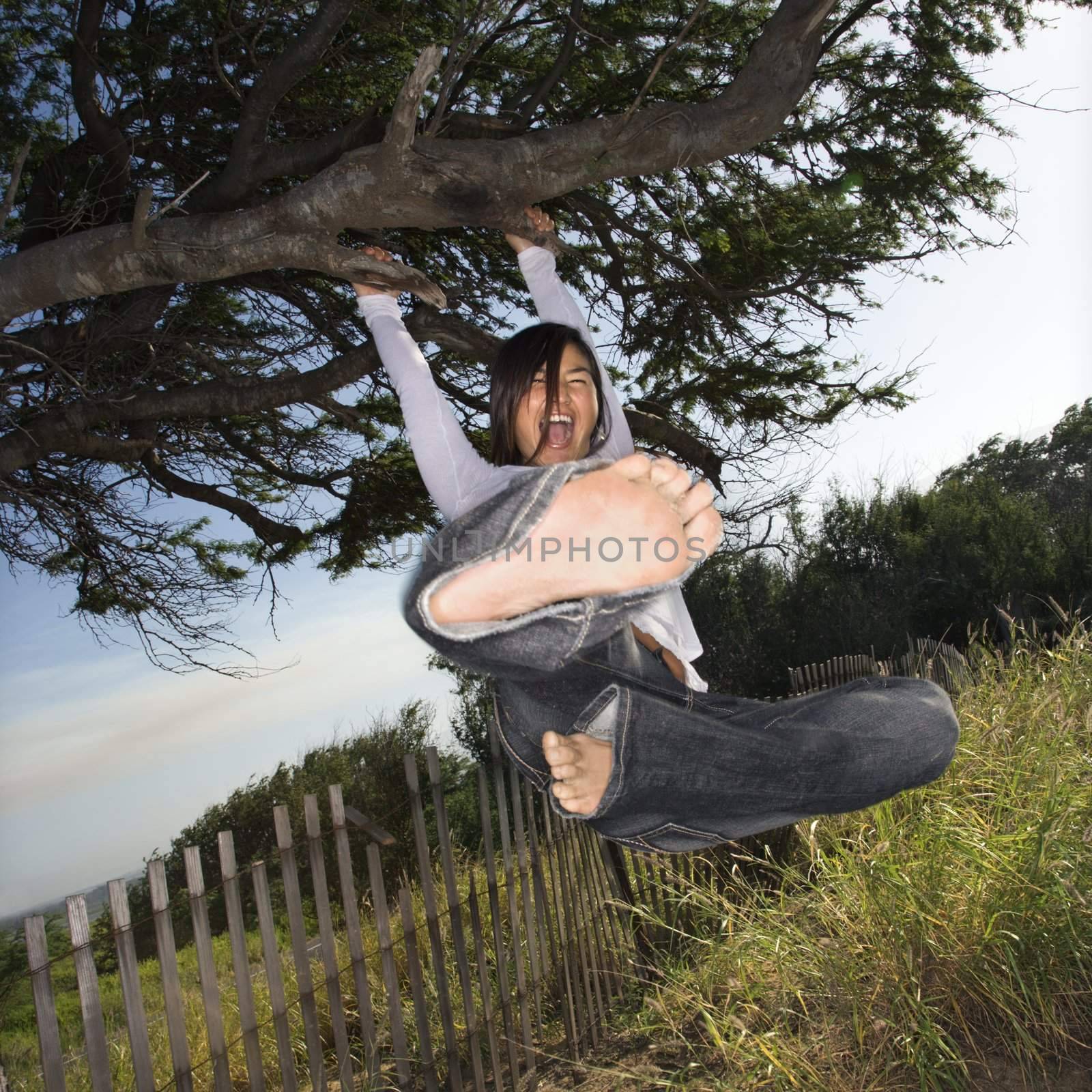 Young adult Asian female holding on to a tree and kicking towards viewer.