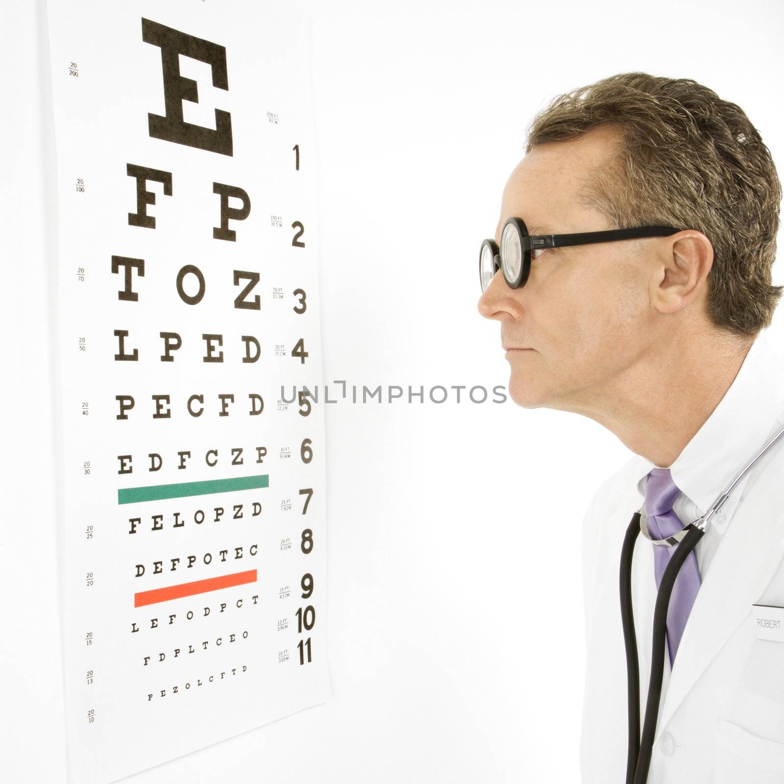 Mid-adult Caucasian male doctor wearing eyeglasses looking at an eye chart.