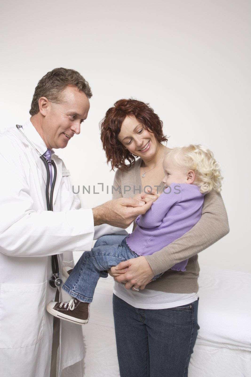 Middle-aged adult Caucasian male doctor comforting Caucasian female toddler.