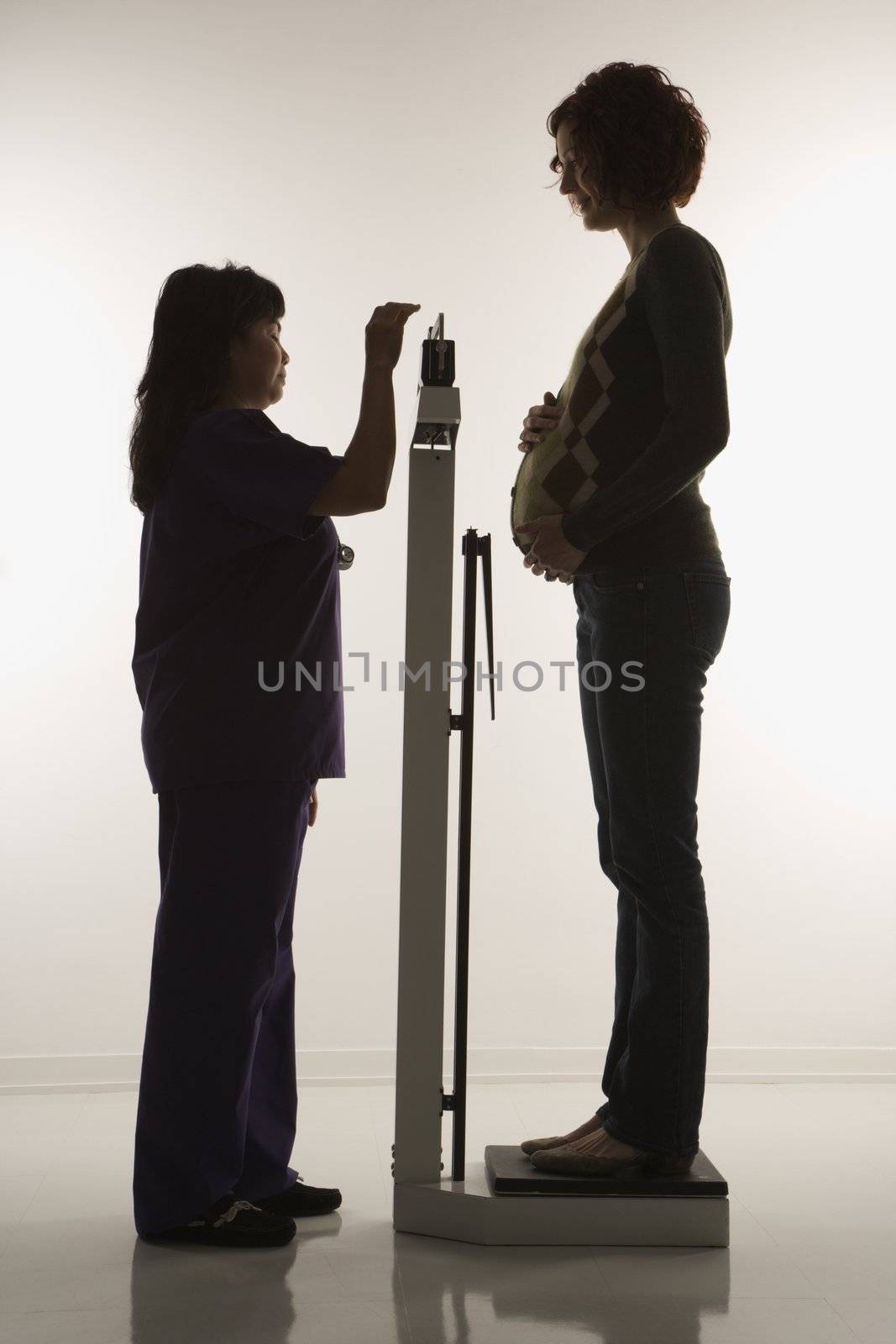 Pregnant Caucasian mid-adult woman being weighed by nurse.