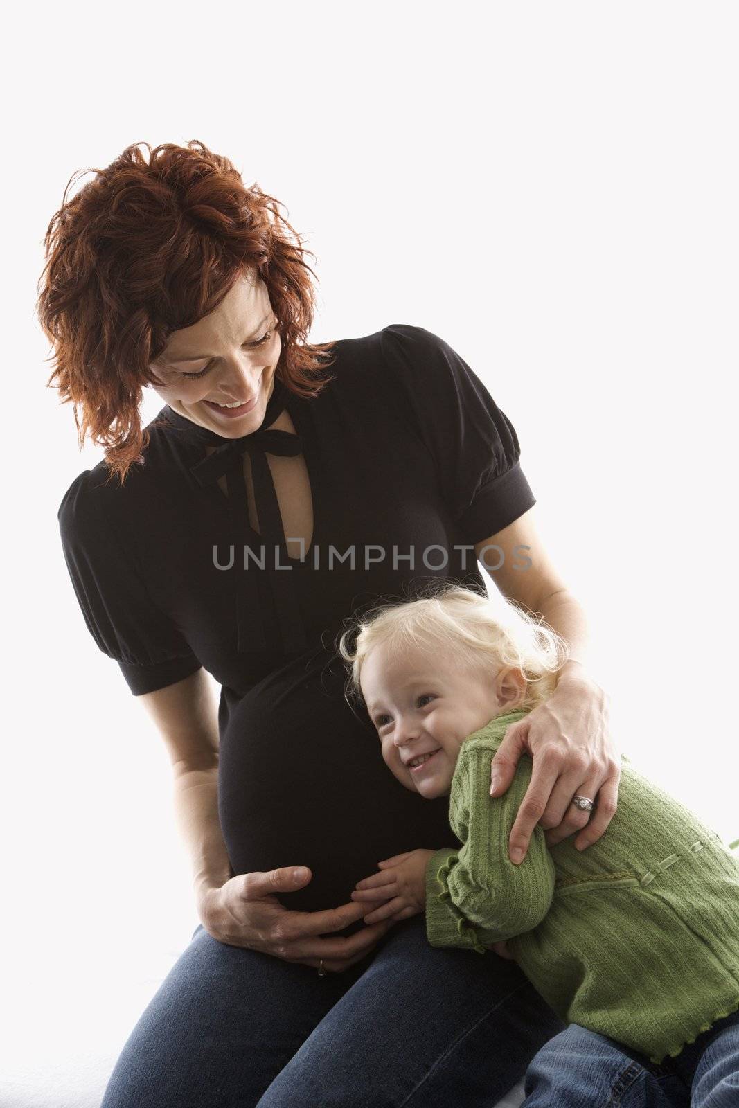 Young Caucasian female child with ear against her mother's pregnant belly.