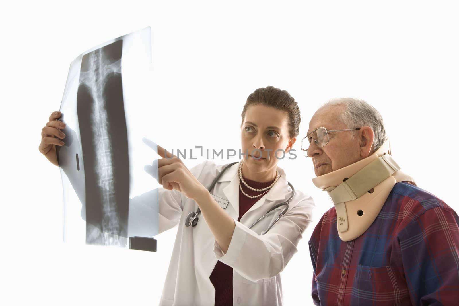 Mid-adult Caucasian female doctor ponting at x-ray with elderly Caucasian male in neck brace looks on.