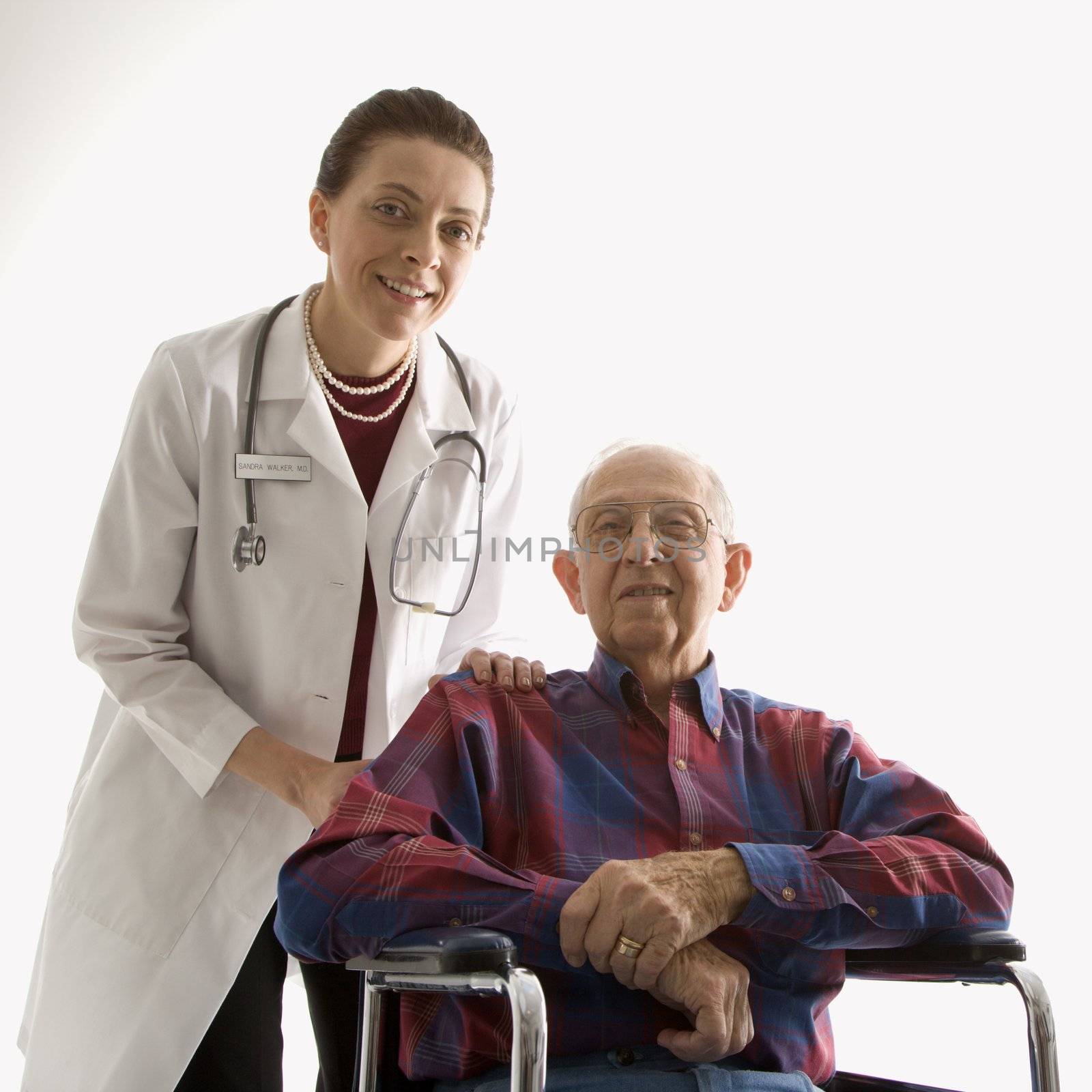 Mid-adult Caucasian female doctor with hands on elderly Caucasian male's shoulder in wheelchair.