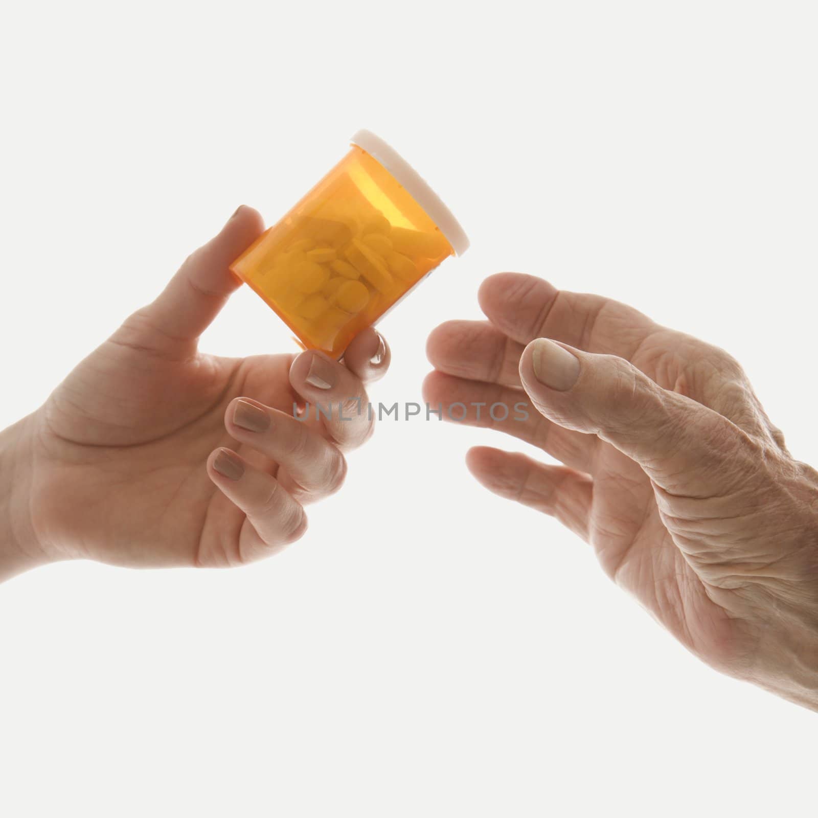 Close-up of mid-adult Caucasian female's hand handing medication bottle to elderly Caucasian male hand.