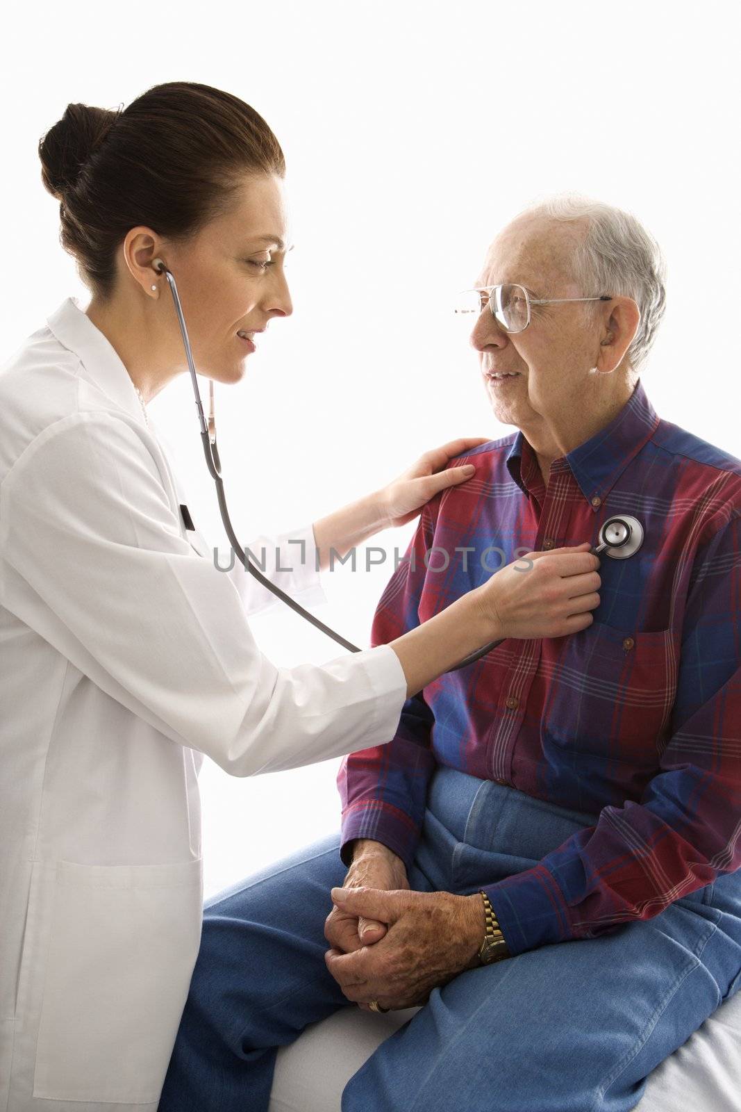 Mid-adult Caucasian female doctor listening to elderly Caucasian male's heart with stethoscope.