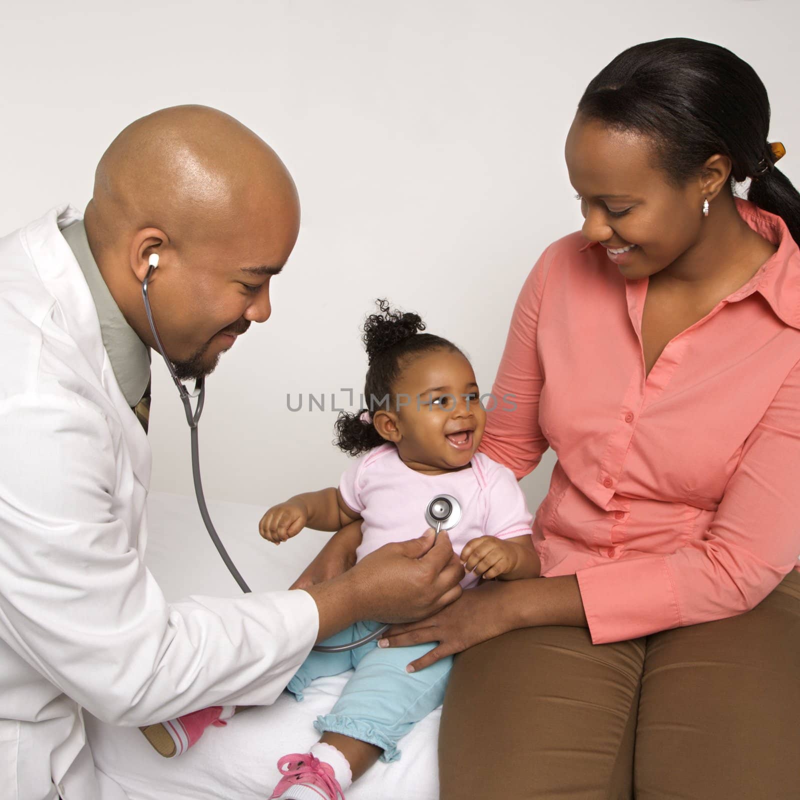 African-American male doctor examining baby girl with mother watching.