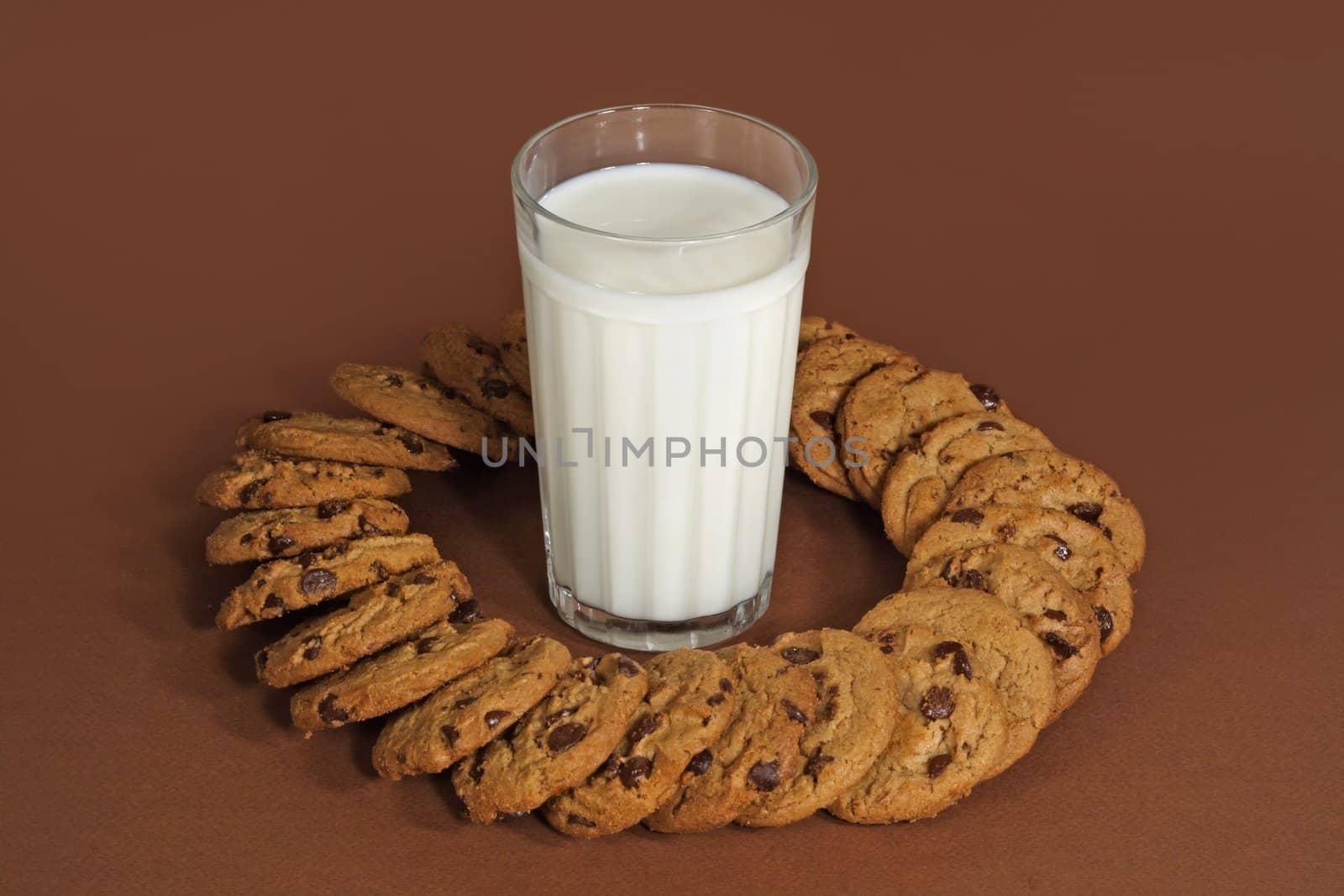 glass of milk and chocolate chip cookies on brown background
