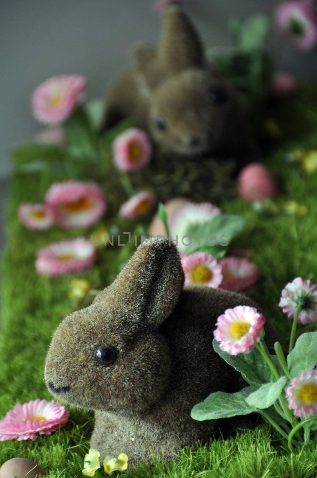 Easter decoration with rabbits, eggs and daisies on faked grass..