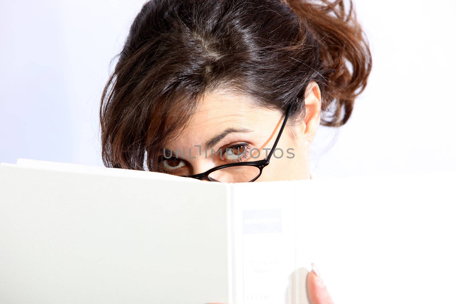 A young woman hides behind a folder / book and peeps away, frowning on the Folder