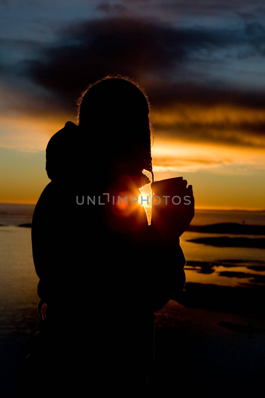 A person standing by the Ocean drink a warm drink at sundown