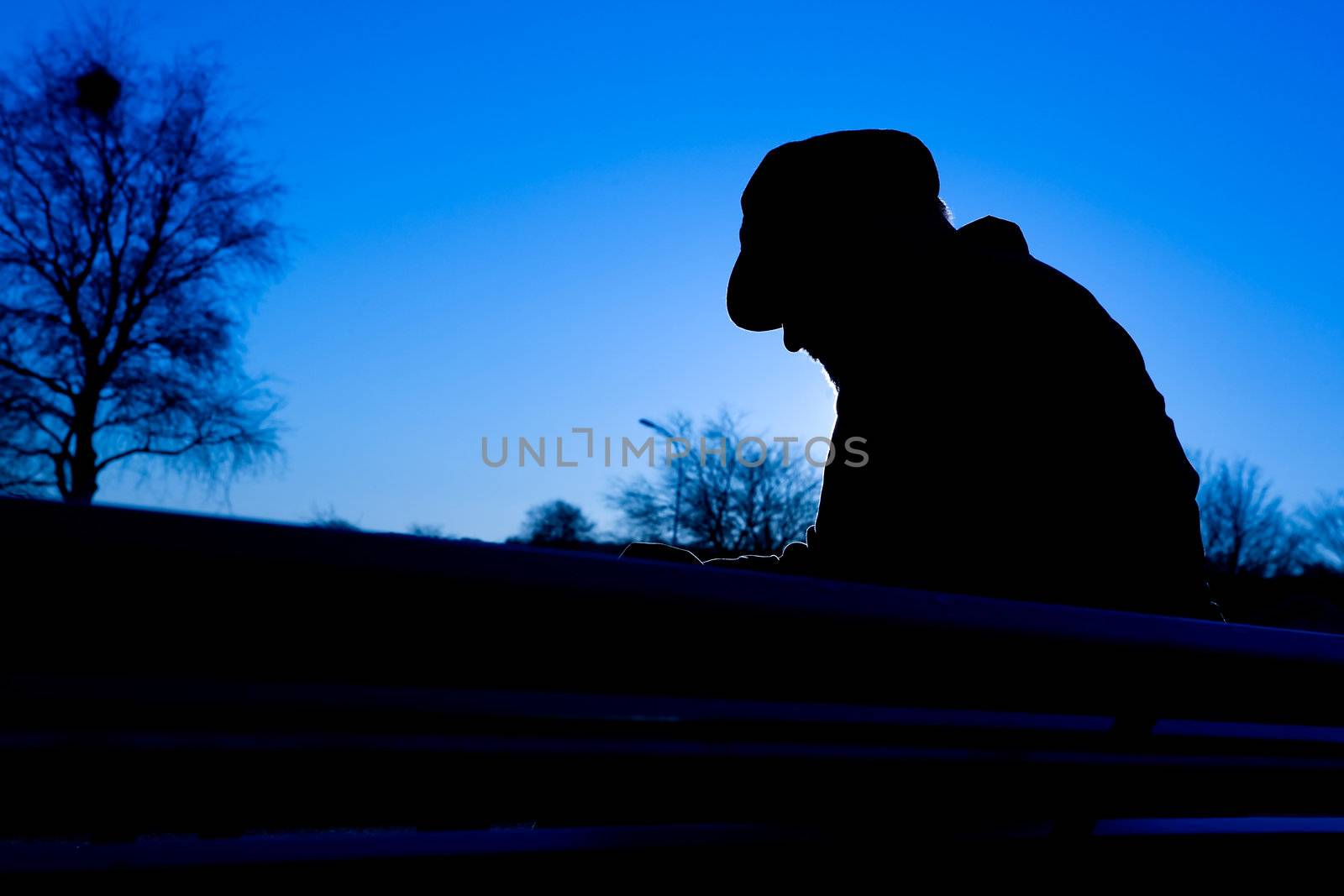 A depressed thoughtful sitting on a park bench in cold winter scene.