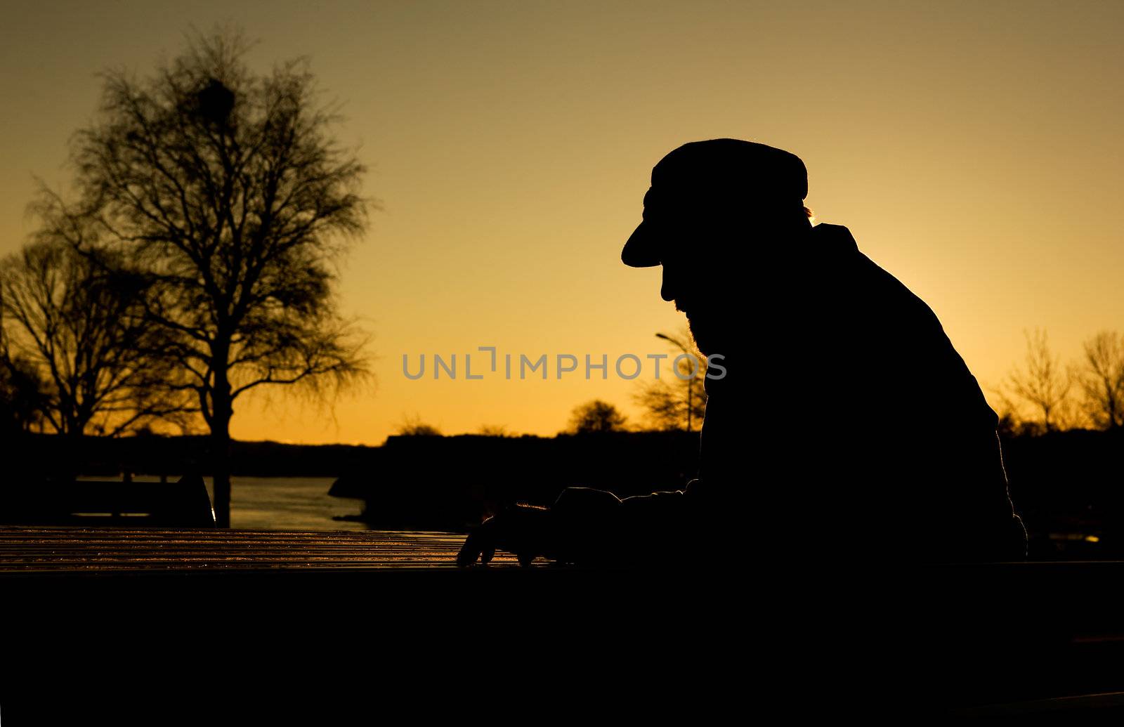 A depressed thoughtful man by the water at sundown.  Warm sunlight creating a silhouette.