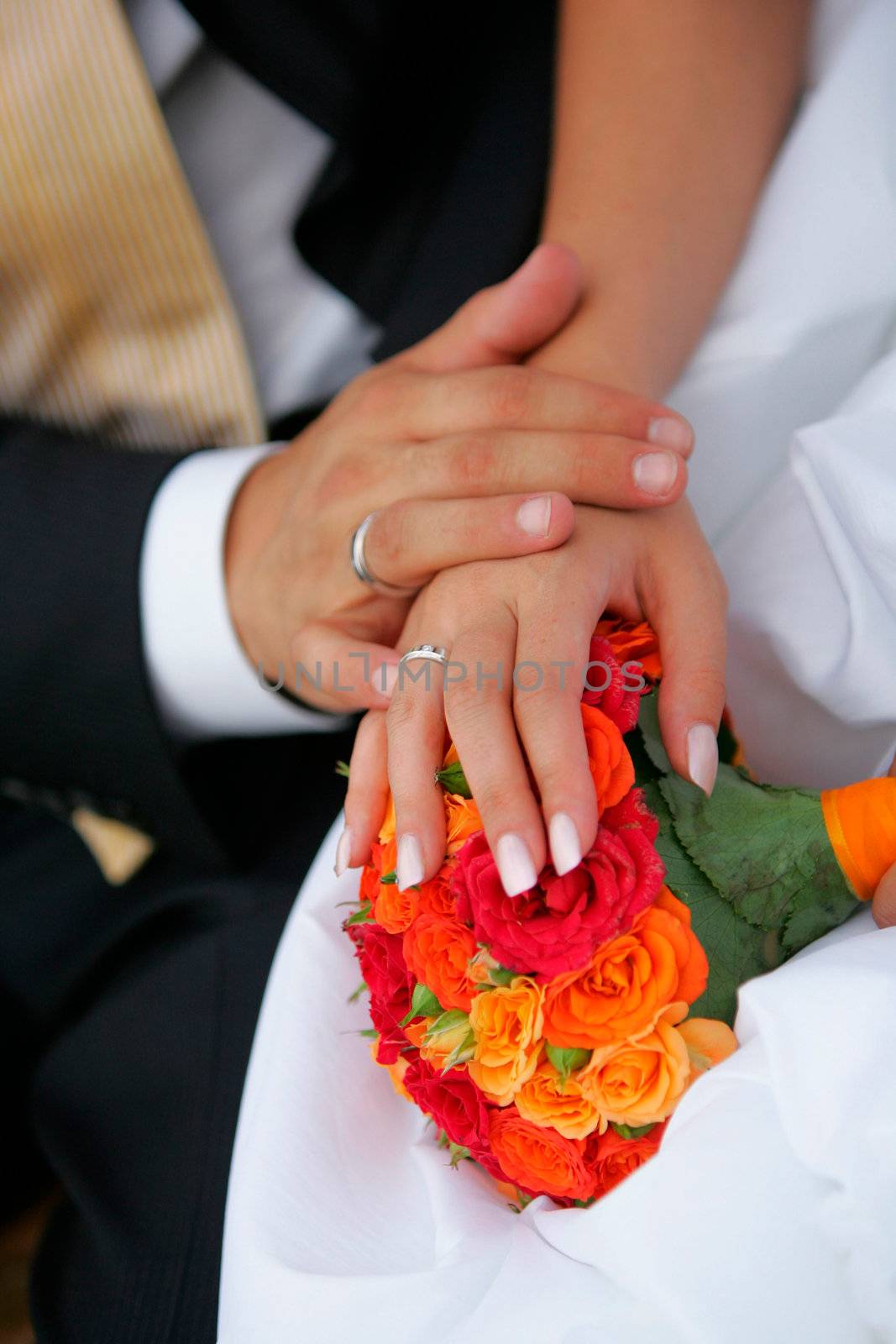 Close up portrait of newlywed man and wife holding hands over bouquet of colorful flowers and petals.