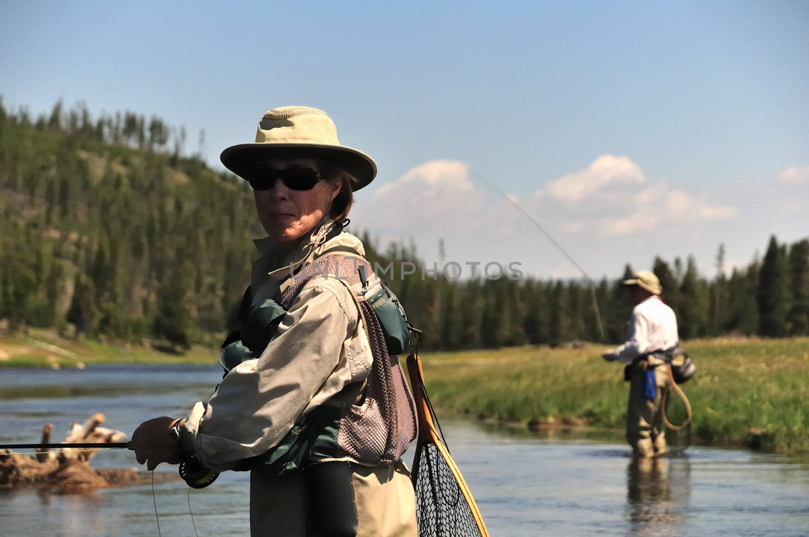 Active senior couple wading in the Firehole River (Yellowstone National Park) and fly-fishing for trout.