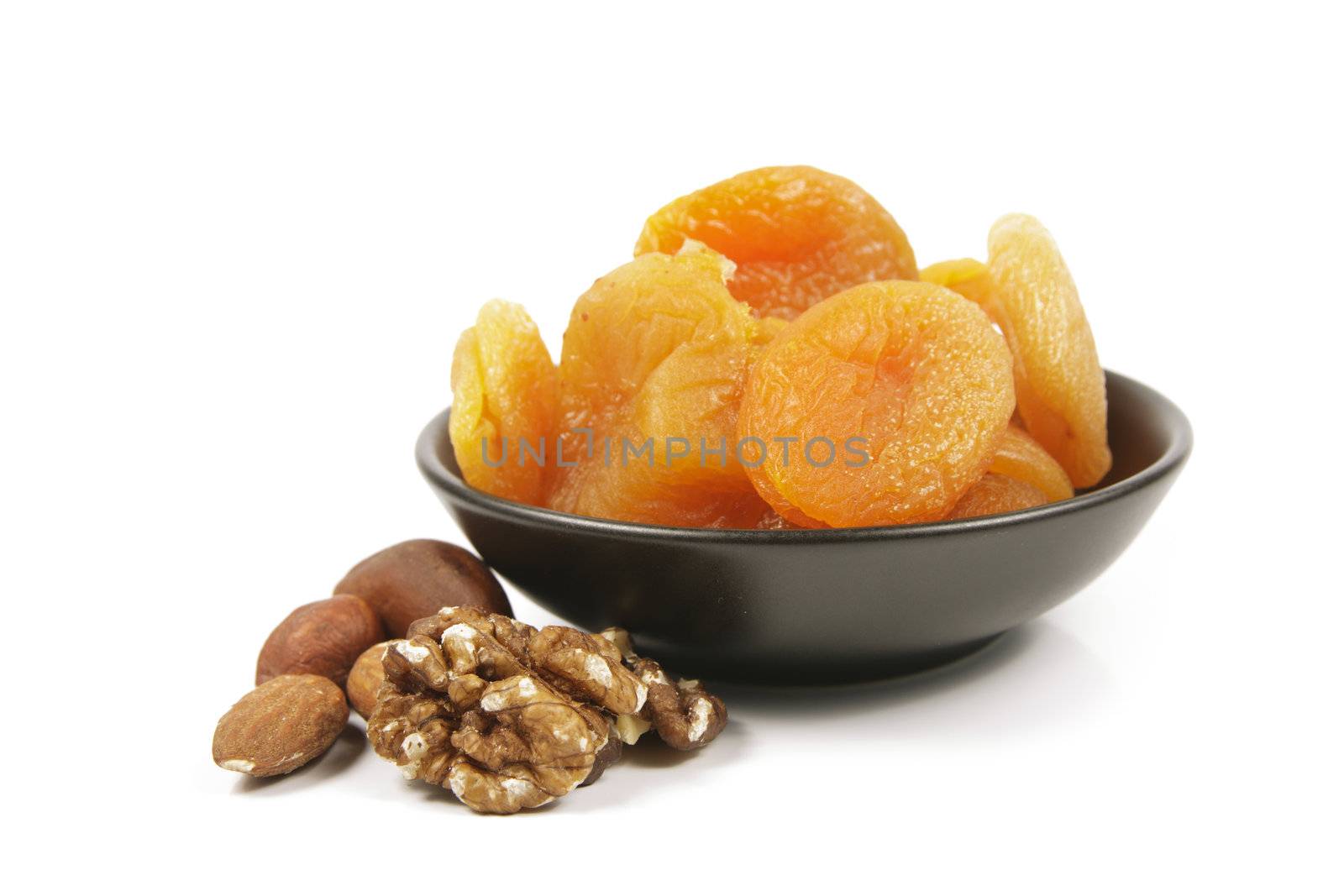 Dried juicy orange apricots with mixed nuts in a small black bowl on a reflective white background