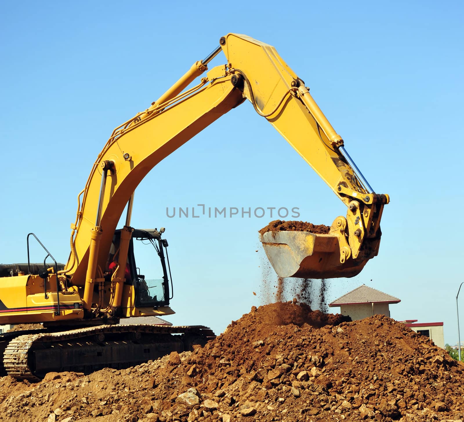 A large yellow excavator moving a large pile of dirt with debris falling from the bucket.