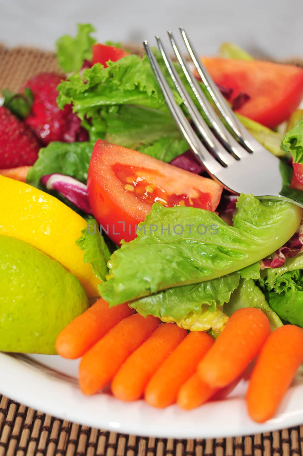 A Lite Salad with a mixture of lettuce, baby carrots, tomatoes with lemon and lime on a white salad plate and designer place mat.