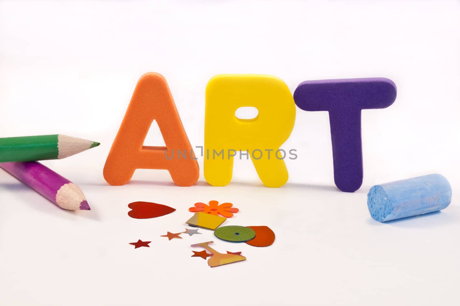 close and low level angle capturing coloured foam letters spelling the word 'ART' arranged over white and surrounded by art and craft materials.