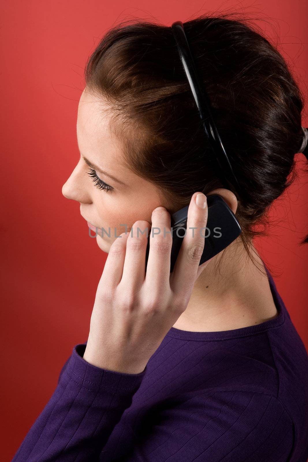 A young female listening on a cell phone. isolated on red.