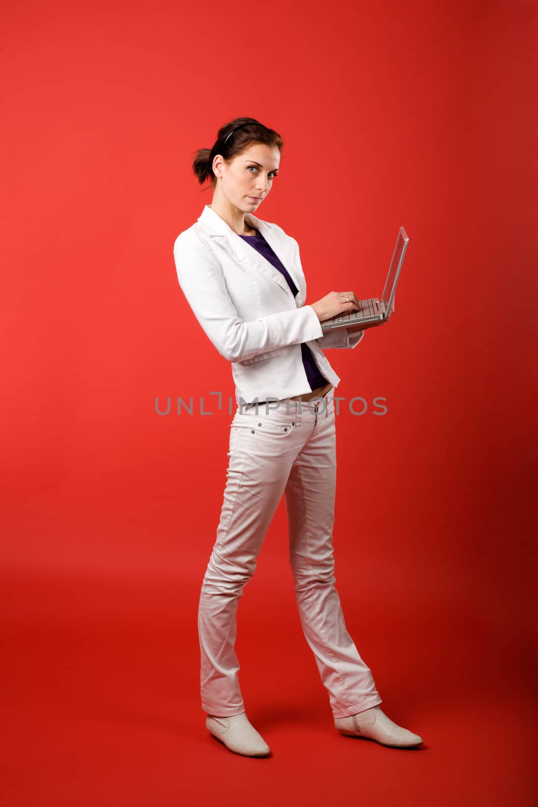 A young woman typing on a laptop computer isolated on red