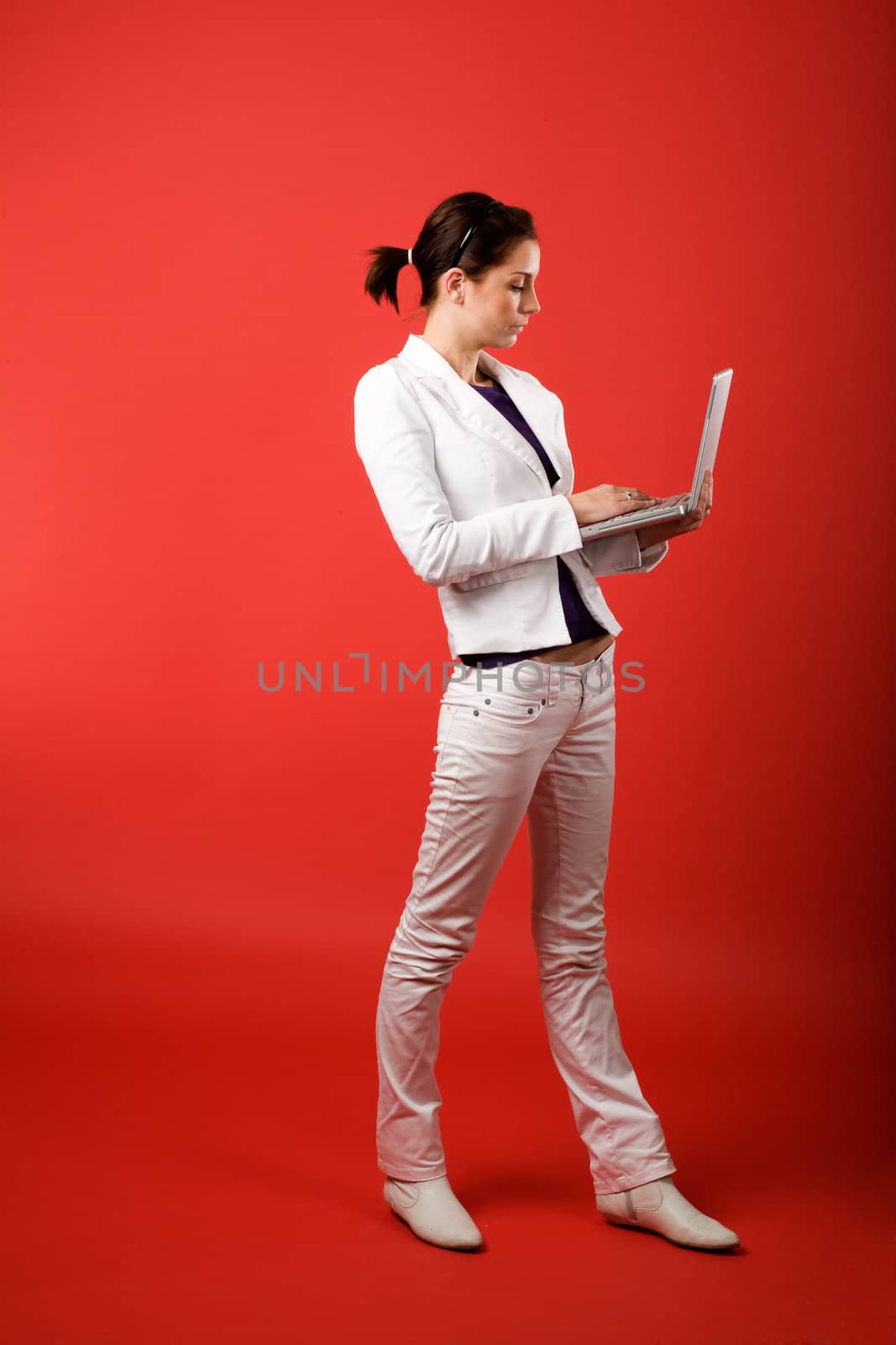 A young woman typing on a laptop computer isolated on red