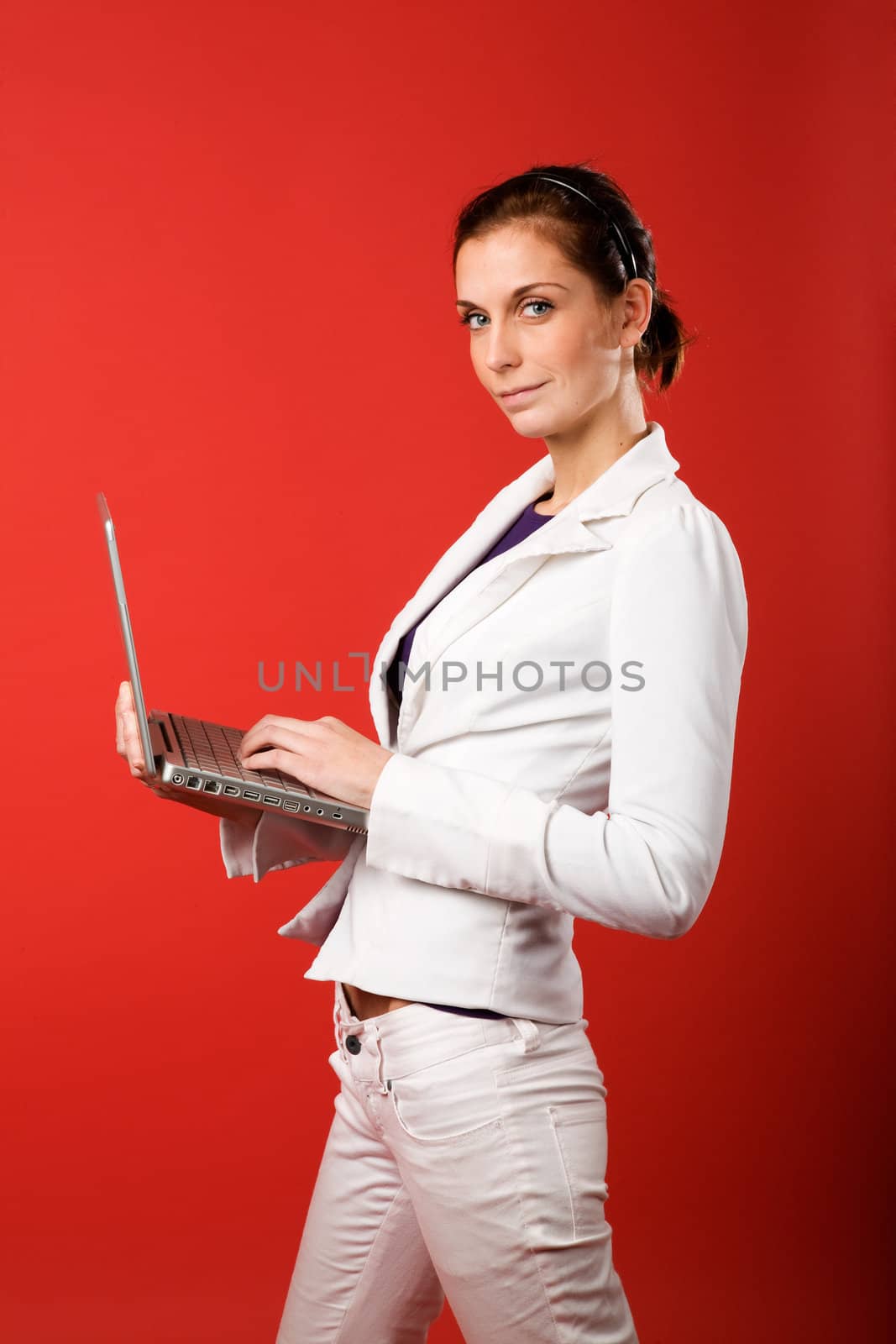 A young woman typing on a laptop computer isolated on red