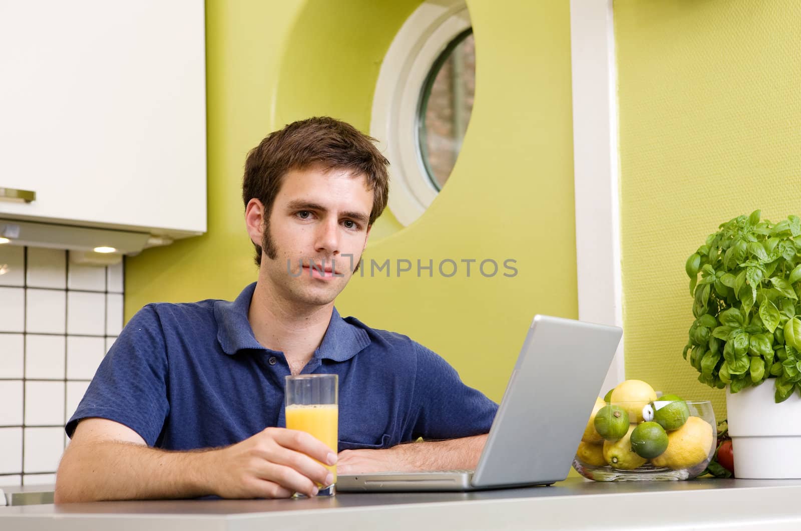 A young male using a laptop computer in the kicthen and smiling at the camera.