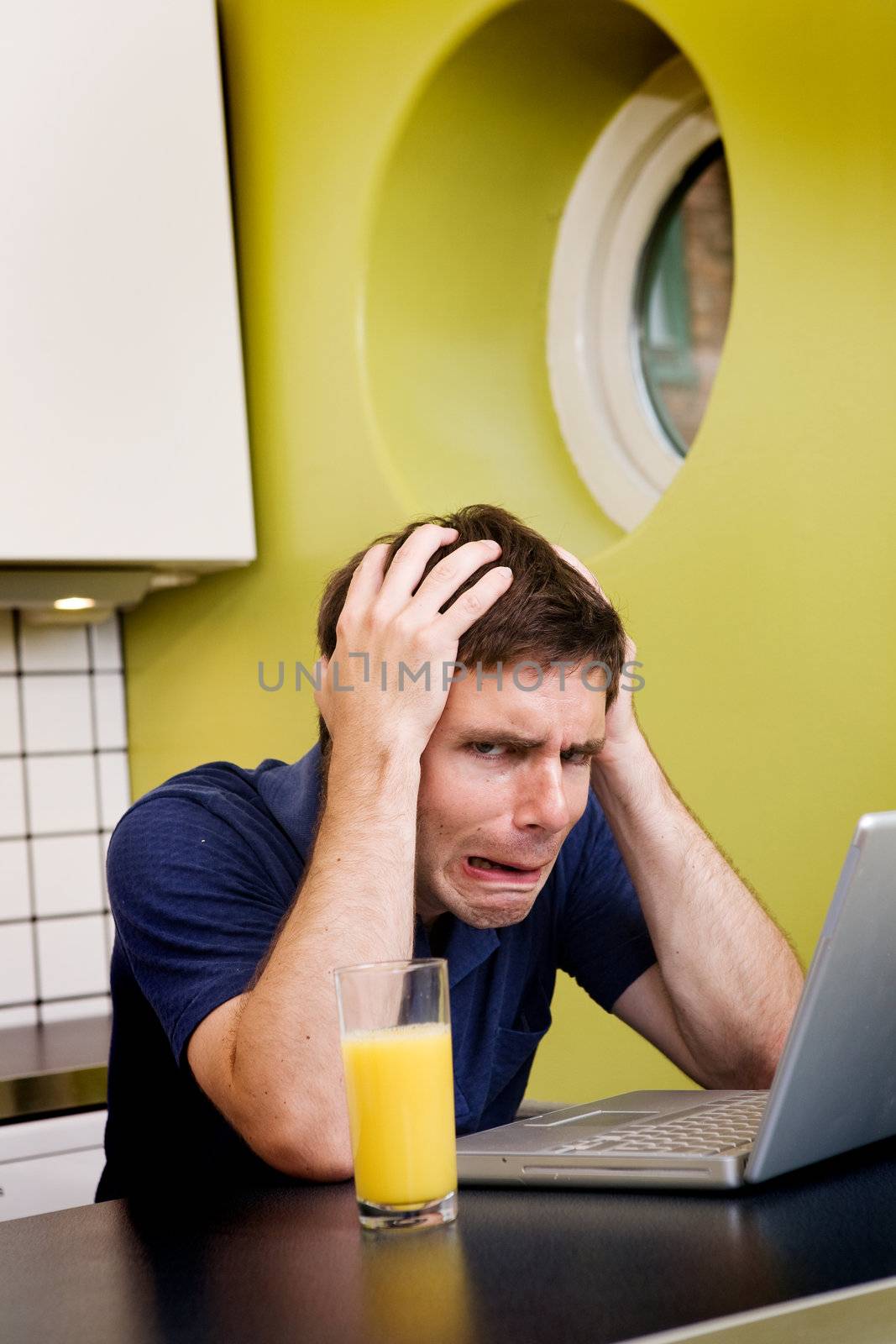 A worried computer user sits in his kitchen with a desperate look on his face